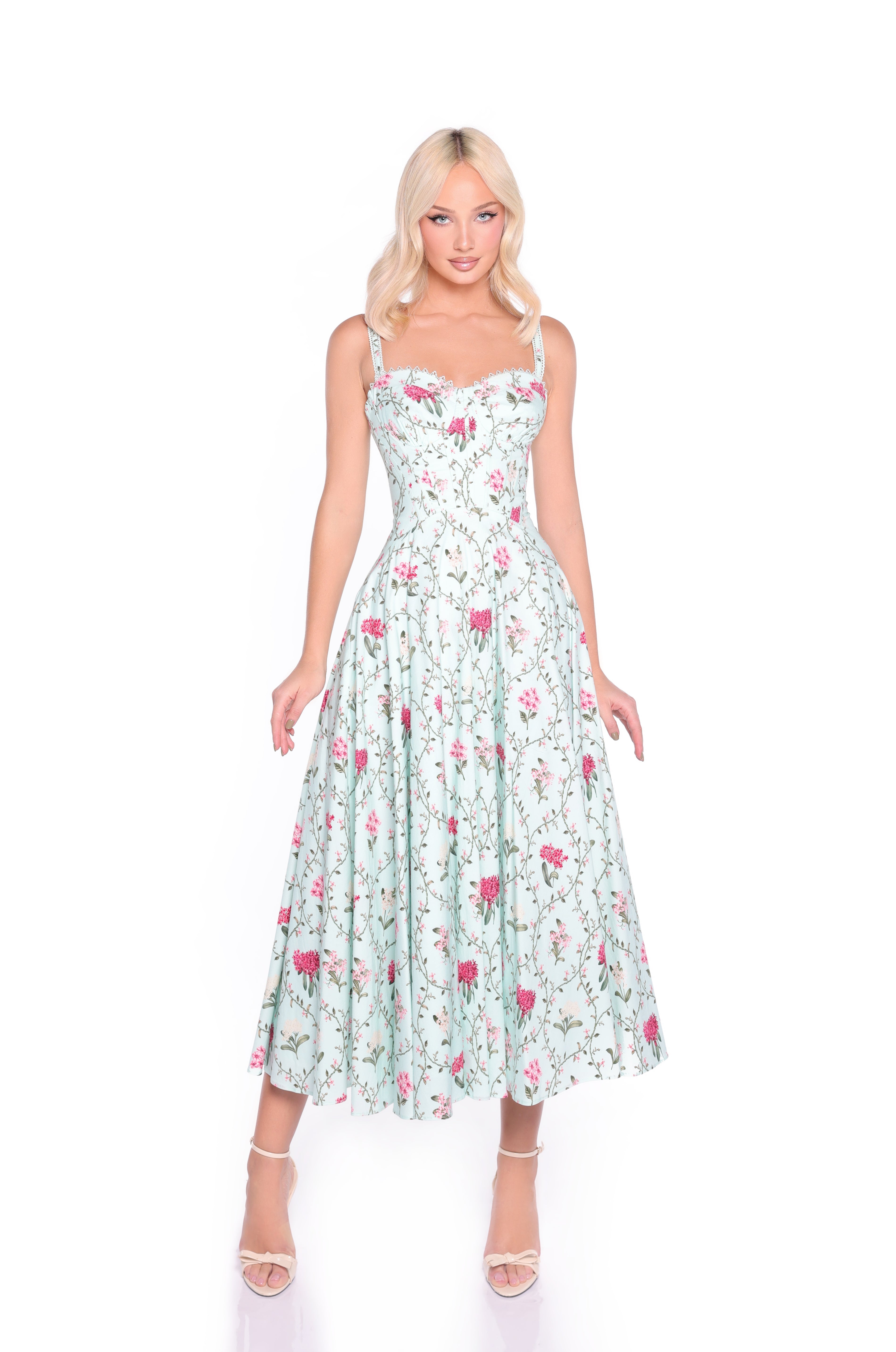 A woman in the Mint Green Floral Casual Midi Dress: Rosella, featuring pink flowers and a corset bodice, paired with nude high-heeled sandals, stands against a plain white background.